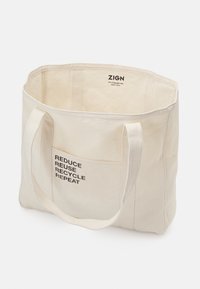 Canvas tote bag in natural color featuring a rectangular shape and short handles. Front displays the text "REDUCE REUSE RECYCLE REPEAT."