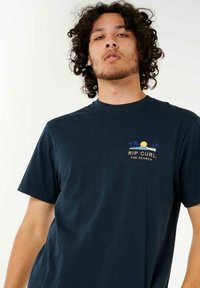 Marineblå bomulds-T-shirt med rund halsudskæring, korte ærmer og et brysttryk af en solnedgang med palmer og tekst.