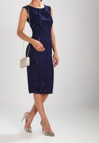 Námořnická modrá šaty s flitry, s přiléhavým střihem a klasickým výstřihem. V kombinaci s metalickou kabelkou a stříbrnými vysokými podpatky. Hladká textura, elegantní design.