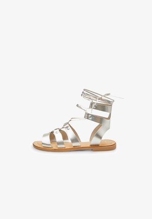 Zilveren metallic gladiatorsandalen zijn voorzien van meerdere banden, een enkelbandje en een platte tan zool met minimale stikseldetails.
