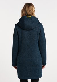 Lång blå kappa med ett strukturerat mönster, huva och sidofickor. Har en logotyp på ärmen och en rak passform.