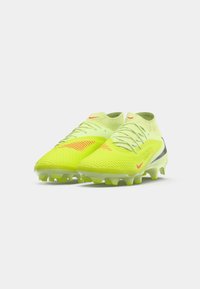 Botas de fútbol de corte alto en amarillo neón con acentos rojos, cordones y suelas con tacos, colocadas una al lado de la otra sobre un fondo blanco liso.