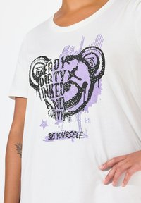 Bílý bavlněný tričko s černým a fialovým grafickým designem a textem, včetně "NERDY," "DIRTY," a "BE YOURSELF," se třpytivými detaily.