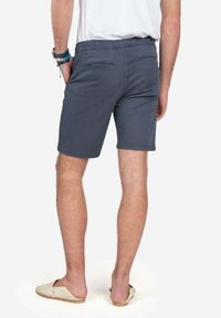 Pantalones cortos de algodón grises con cinturilla elástica y dos bolsillos traseros. Textura suave, hasta la rodilla y combinados con zapatos slip-on ligeros.