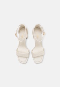 Krämfärgade fusk läder klacksandaler med fyrkantiga tår, två framremmar och en ankelsnodd med detaljer i guld.