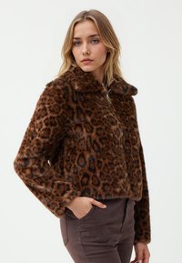 Brązowa kurtka z sztucznego futra w leopardzie wzór, z zapięciem na zamek i wysokim kołnierzem. Posiada długie rękawy i krótki fason.