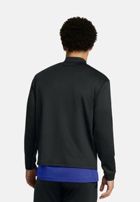 Black athletic jacket with a stand-up collar, long sleeves, and smooth texture. Worn over a blue shirt; minimal design and no visible logos.