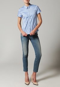 Chemise bleu clair à manches courtes avec boutons, en tissu de coton, associée à un jean skinny bleu délavé et des escarpins couleur nude.