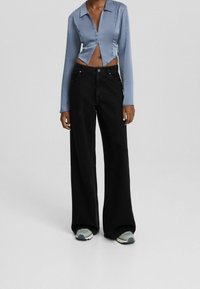 Avklippt blå satin skjorta med långa ärmar, parat med vida svarta jeans och grå sneakers. Har knäppning framtill och fickor.