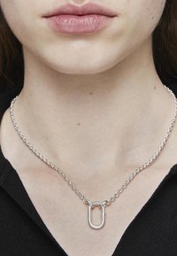 Collar de cadena de plata con un colgante de eslabón ovalado, con una textura suave y un diseño minimalista. Llevado en el cuello, ajustado.