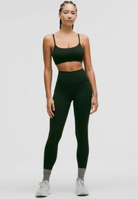 Sujeción deportiva de color verde oscuro y leggings de cintura alta. Textura suave, diseño minimalista, con tirantes finos y construcción sin costuras.
