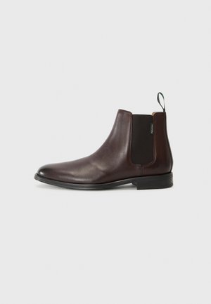 Bottines en cuir marron avec des panneaux élastiques sur les côtés et une languette. Texture lisse, bout rond et un petit talon empilé.