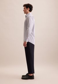 Hellblaues Button-up-Hemd aus leichtem Stoff, mit langenÄrmeln und abgerundetem Saum. Getragen mit maßgeschneiderten dunklen Hosen und schwarzen Schuhen.