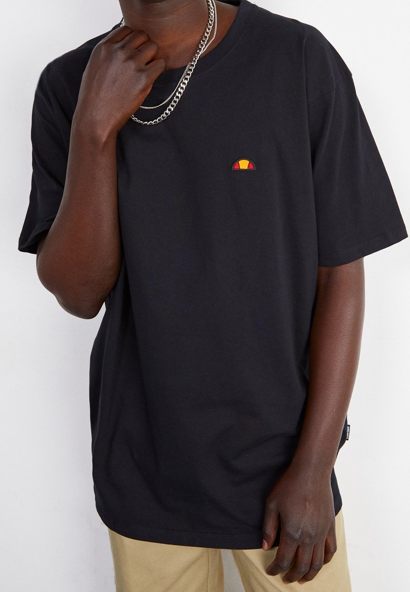 T-shirt en coton noir avec un col rond, arborant un petit logo brodé rouge et jaune sur la poitrine et des manches courtes.