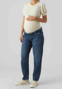 Gravidkläder med en ribbad krämfärgad topp med puffärmar och blå denimjeans med elastisk midja. Vita sneakers fulländar looken.