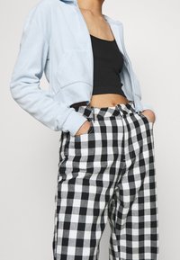 Giacca a zip cropped blu chiaro realizzata in materiale morbido, abbinata a pantaloni a vita alta in gingham bianco e nero con tasche laterali.