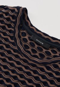 Haut texturé avec un design ondulé en bleu foncé et beige, col rond et étiquette affichant "OPUS". Tissu doux et extensible.
