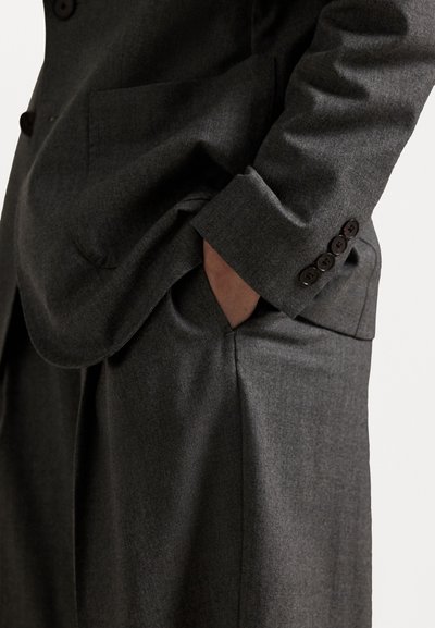 Gray tailored suit with a textured fabric, featuring a single chest pocket, visible buttons on the cuff, and relaxed fit trousers.