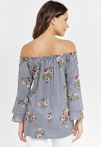 Off-shoulder topp med blå och vita ränder samt blommönster. Har bjällersärmar och en rynkad halsringning för extra detaljer.