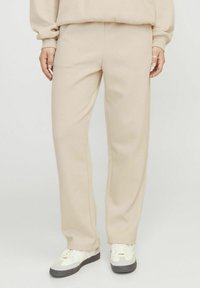Pantalones de chándal beige hechos de una tela suave, diseño de pierna recta, con cintura elástica, presenta costuras mínimas y se combinan con zapatillas blancas.