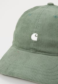 Zöld kordbársony baseball sapka lekerekített koronával, varrott részletekkel és egy fehér hímezett logóval az elején.