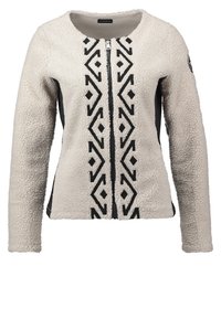 Bluza polarowa w kolorze ecru z czarnym geometrycznym wzorem z przodu, zamkiem błyskawicznym i kontrastującymi czarnymi panelami po bokach. Miękka w dotyku.