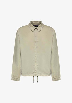 Veste beige clair à manches longues avec col, fermeture à pression devant, poignets élastiques et ourlet réglable par cordon.