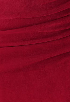 Punane kangas, millel on voldid ja pehme, tekstuuriga pind, paigutatud lainetesse, luues sügavust ja visuaalset huvi.