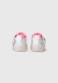 Zapatillas plateadas iridiscentes para niños con un brillante forro interior rosa y suelas translúcidas, vistas desde atrás sobre un fondo liso.