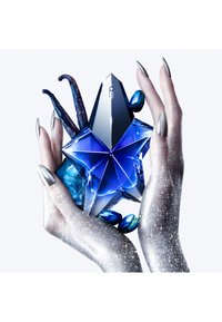 Botella de perfume de vidrio azul en forma de estrella, sostenida entre manos metálicas brillantes, rodeada de acentos azules y elementos texturizados.