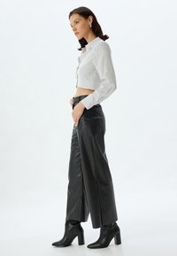 Witte cropped shirt met verticale zwarte strepen, gecombineerd met hoge zwarte leren wijde broek en enkellaarsjes.