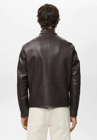 Veste en cuir synthétique marron avec une coupe droite, un col montant et des poignets zippés ; présente une texture lisse et des coutures minimalistes.