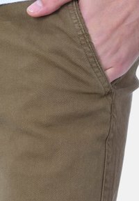 Pantaloni di cotone marroni con una texture liscia, vestibilità slim e una tasca laterale con dettagli di cucitura sottili.