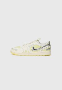 Baskets Nike basses en crème et jaune pâle avec logo Swoosh argenté métallique et détails en mesh à motifs sur fond blanc.