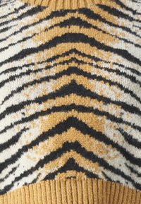 Pull en maille avec un motif rayé tigre en noir, doré et crème, avec un ourlet en ribbes jaune moutarde et une texture douce.