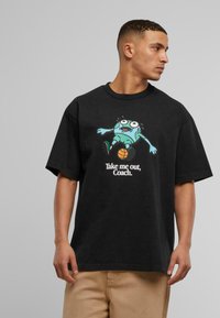 Camiseta de algodón negra con un gráfico de dibujos animados de un personaje azul con ojos grandes, texto "Llévame afuera, entrenador," y mangas cortas.