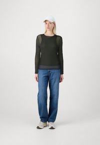 Svart långärmad topp med genomskinliga meshpaneler, kombinerad med högmidjade blå jeans och vita sneakers, samt en vit keps.