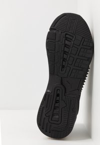 Schwarze Athletikschuhsohle mit strukturierten Mustern, Rillen und einem markanten Logo. Leichtes Gummi-Material sorgt für Grip und Langlebigkeit.