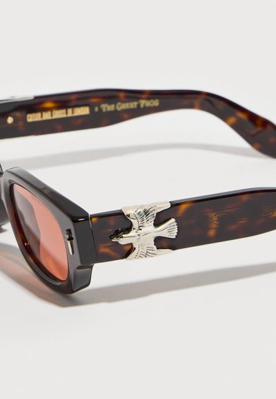 Ορθογώνια γυαλιά ηλίου από τόνους χελώνας με κόκκινα φακούς και ασημένια διακοσμητικά πουλιού στο σκέλος ναΐκλας.