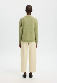 Grüner Wollpullover mit rundem Ausschnitt, langen Ärmeln und geripptem Saum, kombiniert mit weiten cremefarbenen Hosen und schwarzen Slip-on-Schuhen.