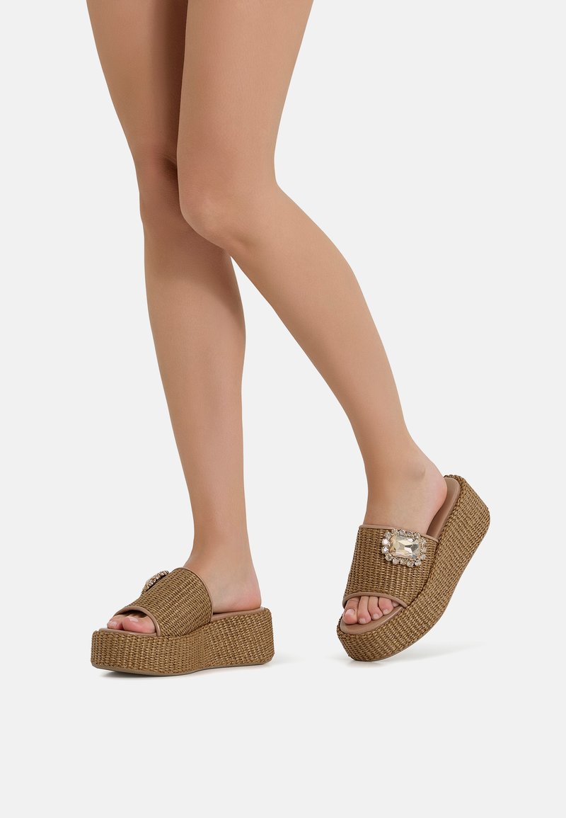 Sandali piattaforma intrecciati marroni con una fascia larga, accenti decorativi di gemme e una suola spessa. Design open-toe, superficie testurizzata.