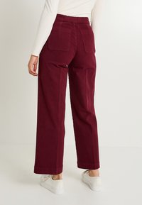 Pantalones de pierna ancha burdeos con un corte relajado, que cuentan con una cintura elástica fruncida y dos bolsillos traseros de parche. Tejido suave y resistente.