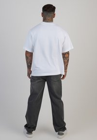 Tricou alb din bumbac cu m�âneci scurte, vedere din spate. Asortat cu pantaloni din denim gri închis, de tip larg, și adidași albi, design minimalist.