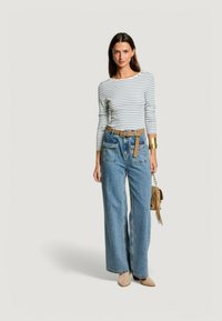 Maglietta a righe a maniche lunghe bianca e blu navy, abbinata a jeans in denim blu a gamba larga. Cintura marrone, scarpe beige e una piccola borsa marrone con nappine.