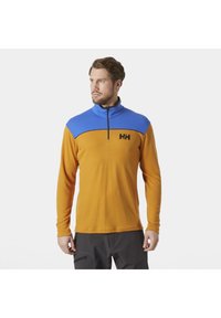 Pomarańczowy pulower z długim rękawem z niebieskim zamek półotwartym przy kołnierzu. Posiada czarną grafikę na piersi oraz dopasowany krój. Gładka struktura.