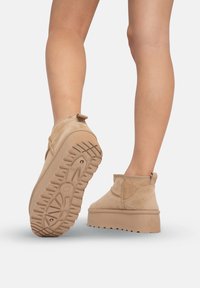 Botines de ante beige con una suela de plataforma gruesa, que cuentan con una parte inferior texturizada y una pequeña lengüeta en la parte posterior.