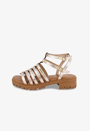 Sandalias de tiras con un acabado metálico en dorado claro, que cuentan con hebillas ajustables, una plantilla acolchada y una suela gruesa y texturizada de goma.