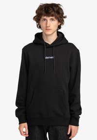Sudadera negra con capucha que presenta un bolsillo canguro en la parte delantera, capucha con cordones y un logo blanco en el pecho. Fabricada con un tejido suave.