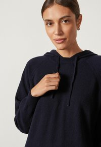 Marineblaues Kapuzensweatshirt aus weichem Material mit lockerem Schnitt, ausgestattet mit einer Fronttasche und Kordeln an der Kapuze.