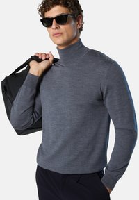 Maglione grigio a collo alto realizzato in materiale morbido, design aderente, maniche lunghe, indossato con una borsa nera. Presenta una superficie liscia e un alto colletto.